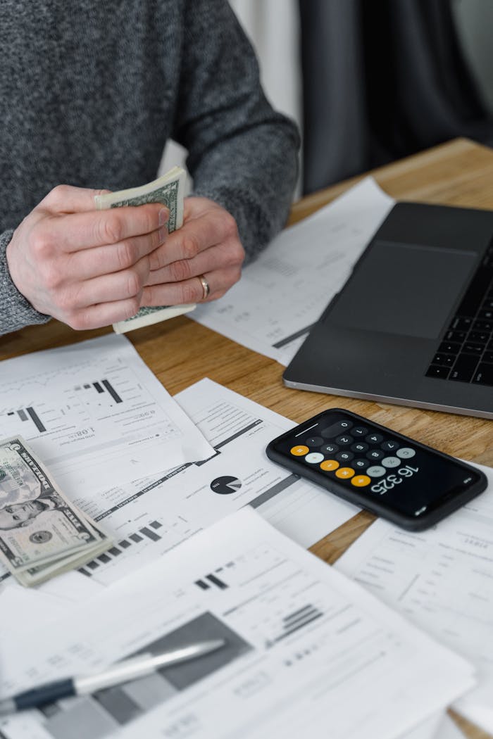 7 Payroll Compliance Risks Every Business Owner Should Know Hands counting money at a workspace with a laptop, calculator, and financial documents.