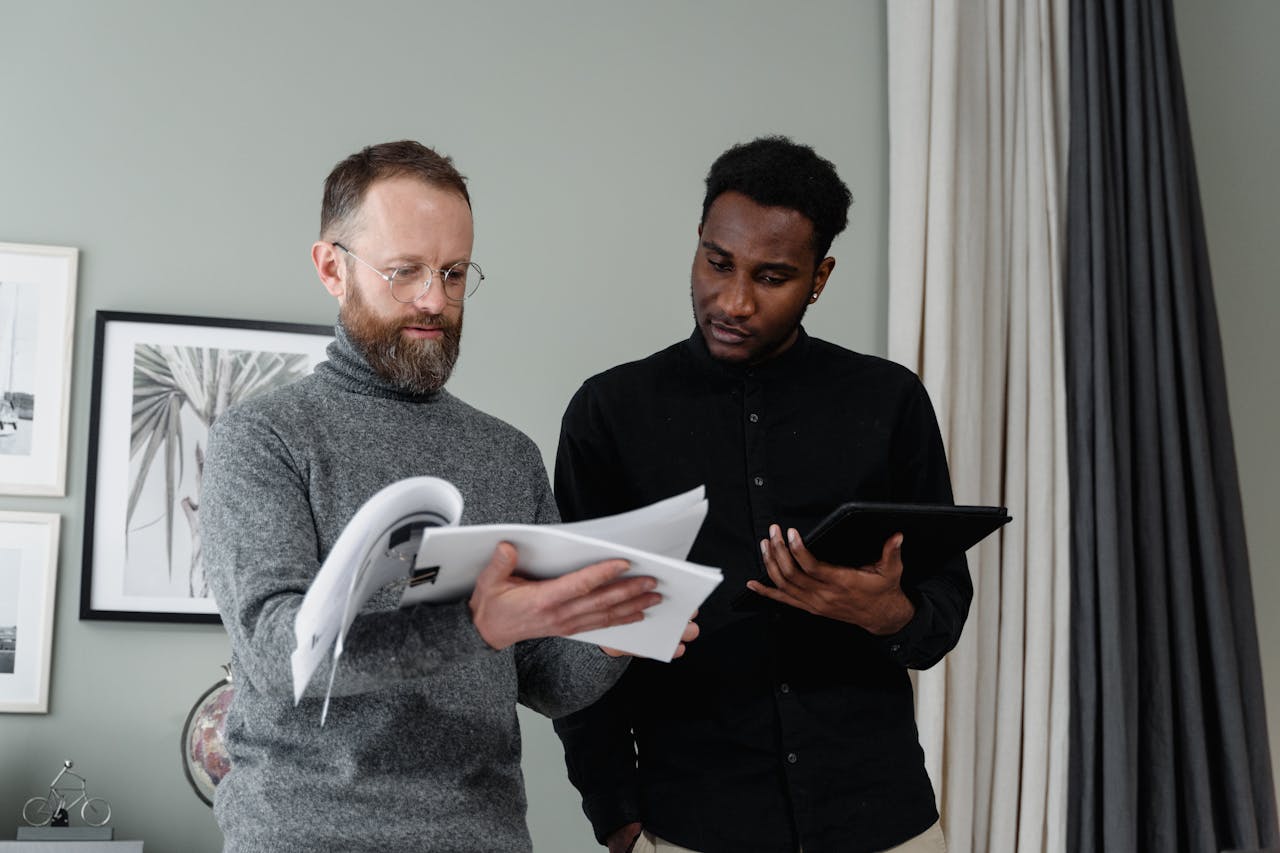 our-story Two businessmen analyzing documents and using a tablet in a modern office setting.