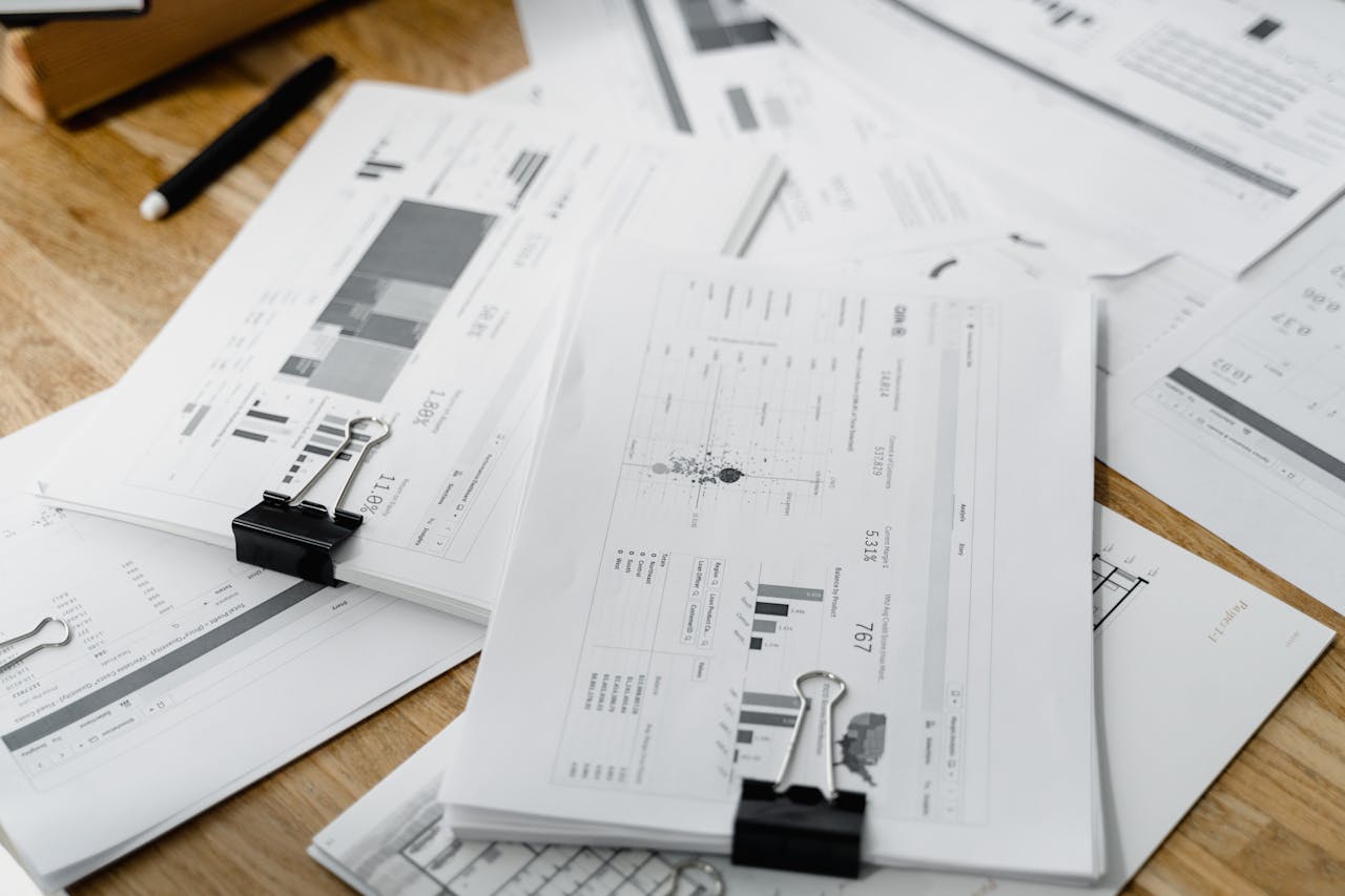 services-01 A stack of financial reports and graphs with clips on a wooden desk, highlighting business planning.